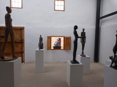 Exposición de escultura en el nuevo taller Esculturas de metal en una galería, con un hombre visible en una ventana al fondo.