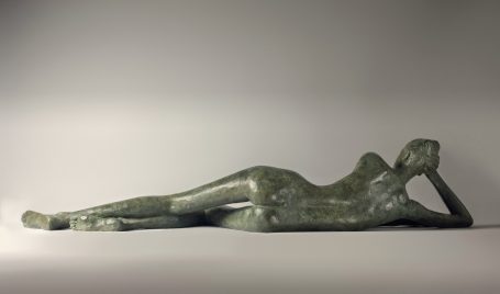 Escultura en bronce de una figura femenina recostada, con una pose relajada y elegante.