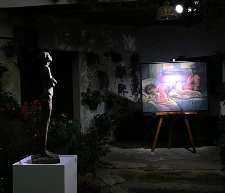 Escultura y cuadro en una galería con luz tenue y plantas alrededor.