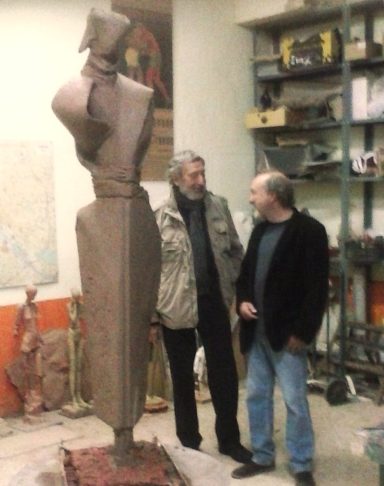 Dos hombres en un taller de escultura junto a una figura de gran tamaño