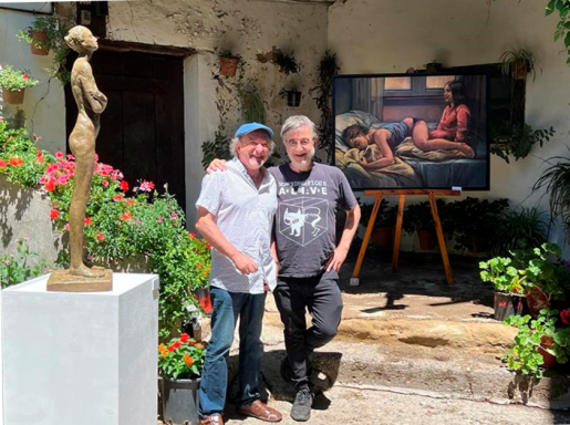 Dos hombres en el jardín de una casa posando para la foto junto a una escultura y un cuadro en el fondo