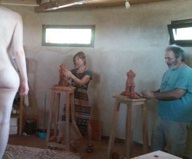 Dos artistas modelan figuras de arcilla en un estudio, con un modelo desnudo de espaldas.