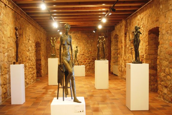 Exposición de esculturas en un museo, con figuras de pie y pedestales iluminados.