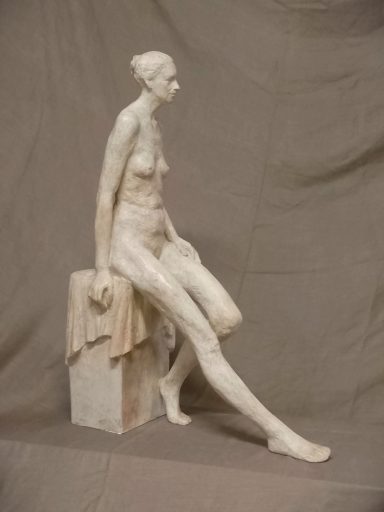 Escultura de una figura femenina sentada, de estilo clásico y acabado en color claro.