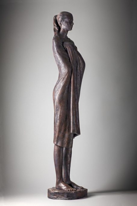 Escultura en bronce de figura femenina de pie, con una vestimenta que cubre su cuerpo.