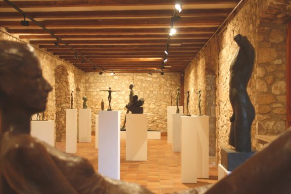 Exposición de esculturas en un museo, con figuras de pie y pedestales iluminados.