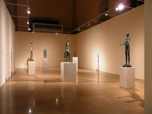 Exposición de esculturas en un museo, con figuras de pie y pedestales iluminados.