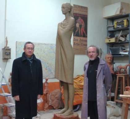 Dos hombres junto a una escultura de una figura femenina mirando al horizonte en un taller de escultura