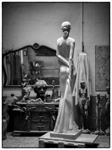 Escultura en blanco y negro de una escultura de piedra que representa una mujer de espaldas en un taller.