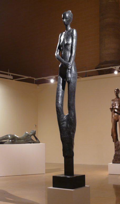 Escultura de figura femenina de bronce, tono oscuro y apariencia estilizada y elegante.