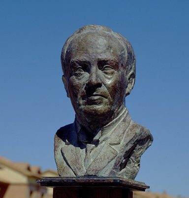 Busto de un hombre con rasgos serios, fondo azul claro.