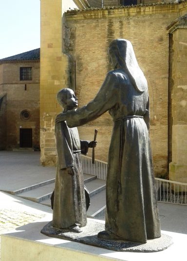 Escultura de una figura adulta y un niño en un entorno urbano.