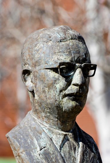 Busto de un hombre con gafas, en un entorno al aire libre.