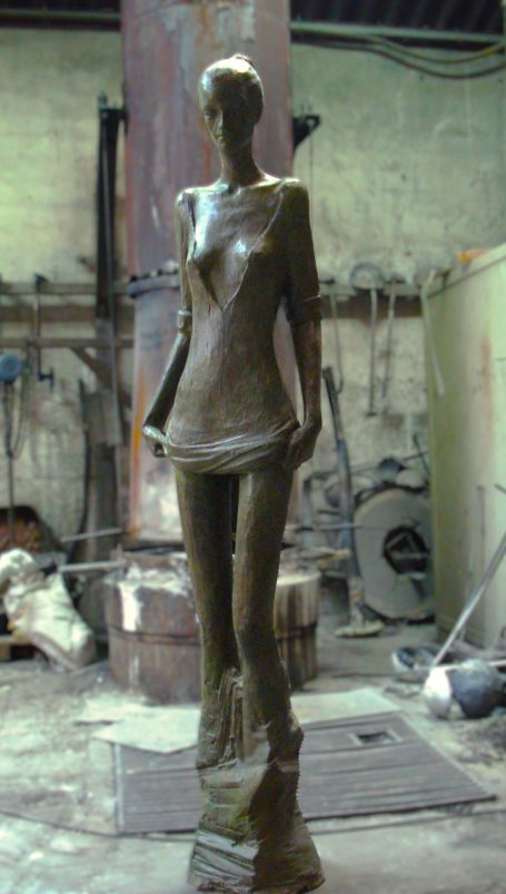 Escultura de mujer de pie, con detalles estilizados y acabado en bronce en un taller de fundición.