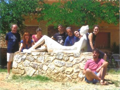 Grupo de personas posando junto a una escultura de figura reclinada sobre una base de piedra.