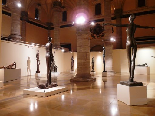 Exposición de esculturas en un museo, con figuras de pie y pedestales iluminados.