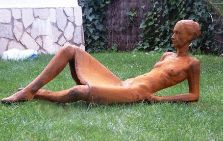 Escultura de figura humana desnuda reclinada sobre césped.