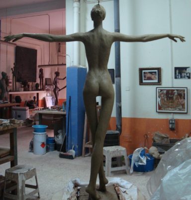 Escultura de figura humana de arcilla en un estudio, vista desde atrás.