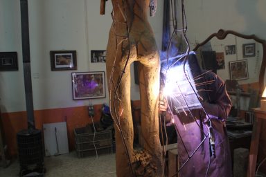 Escultura de madera en proceso, con herramientas y luz eléctrica en un taller.