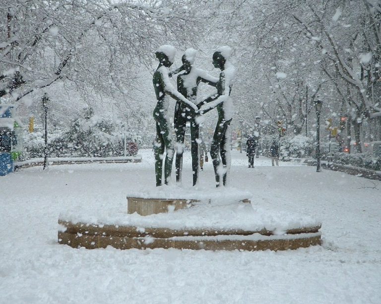 Tres figuras de bronce reunidas en un paseo urbano cubierto de nieve.