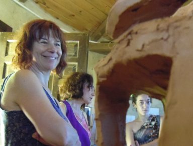 Mujeres sonriendo en un taller de escultura, con una figura de barro en primer plano.