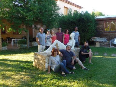 Grupo de personas posando en un jardín con árboles y una escultura en el fondo.