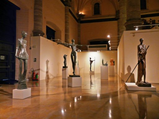 Exposición de esculturas en un museo, con figuras de pie y pedestales iluminados.