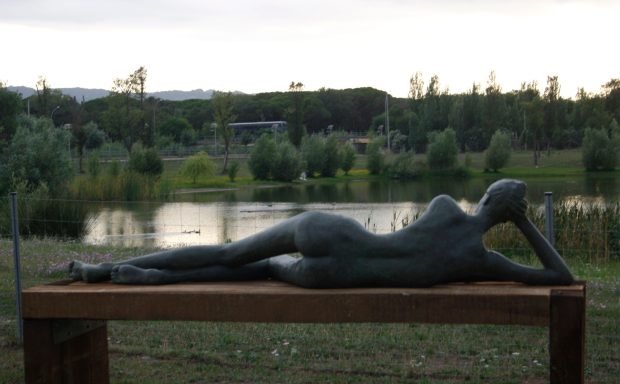 Escultura de una figura femenina recostada sobre una mesa, con un paisaje natural al fondo.