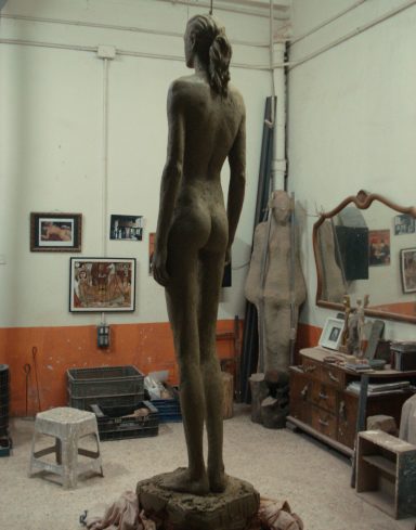 Escultura de una figura humana de pie, vista desde atrás, en un estudio.