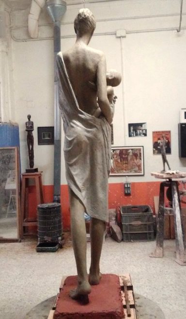 Escultura de mujer de espaldas, sosteniendo a un bebé, vestida con una toga.