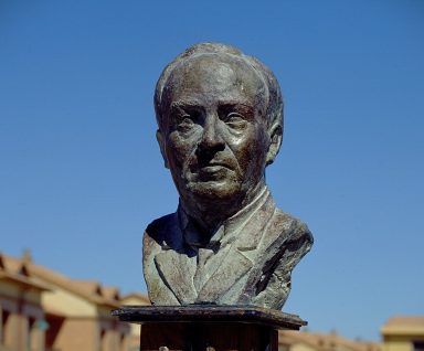 Busto de un hombre con el cielo azul de fondo, en un ambiente urbano.