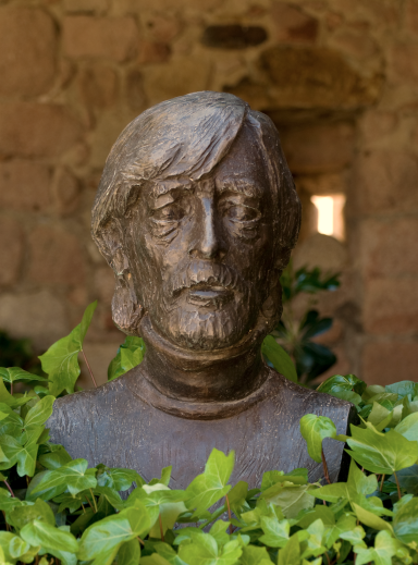 Escultura de busto de un hombre con barba entre hojas verdes.