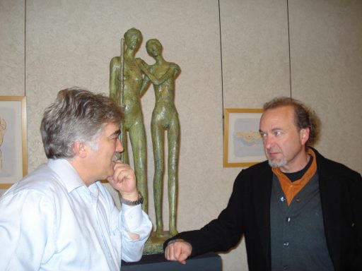 Dos hombres conversando frente a una escultura 