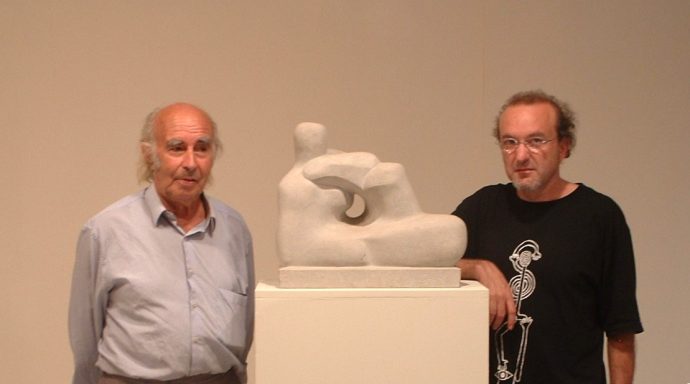 Dos hombres junto a una escultura que representa una figura humana sobre una peana